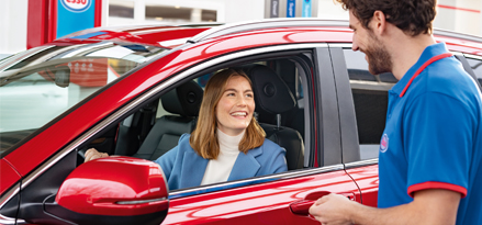 Woman in red car talking to male staff at station.